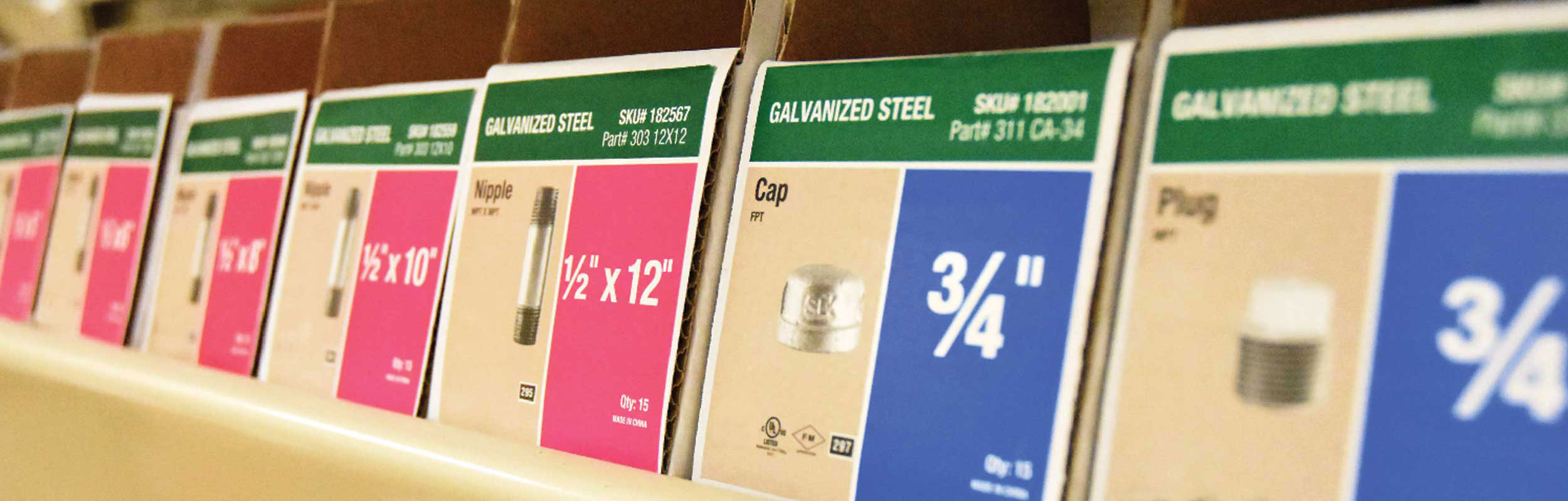 Boxes of galvanized steel plumbing fittings including nipples, caps, and plugs in various sizes lined up on a shelf.